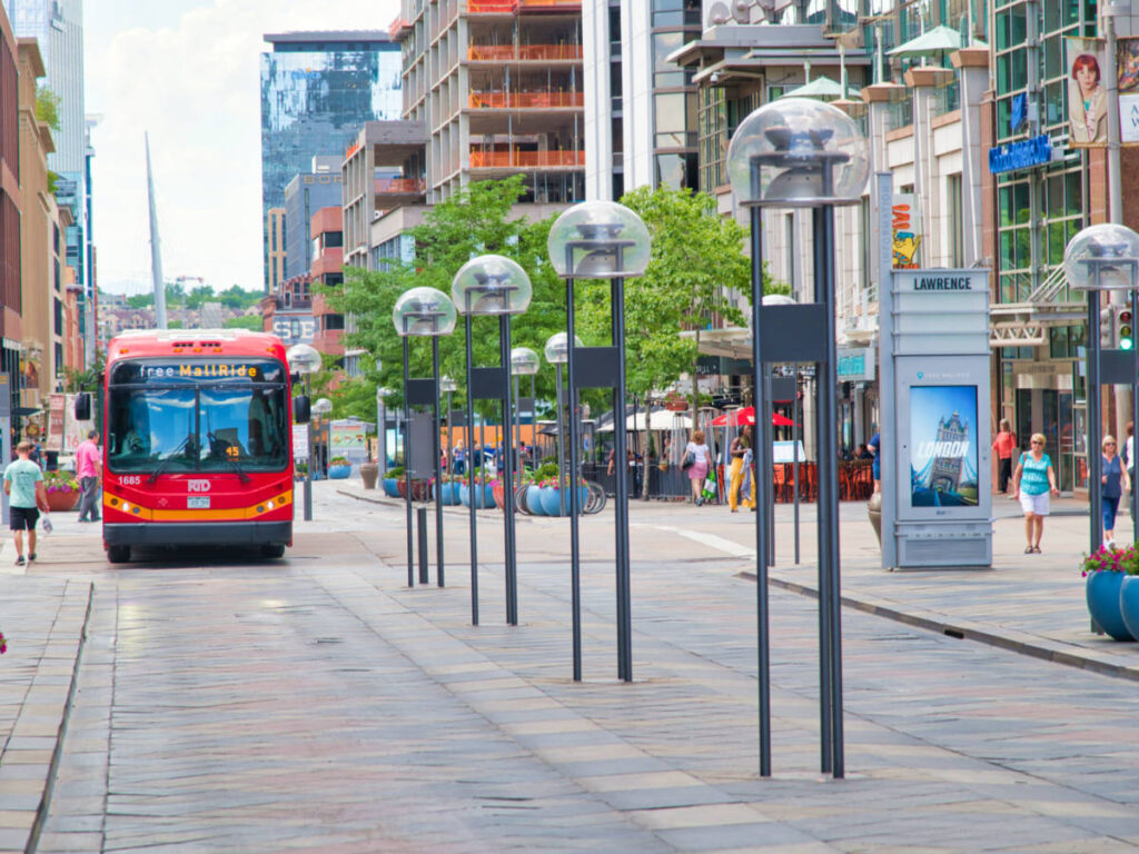 A red bus driving down a street, surrounded by buildings and pedestrians at 16th Street Mall