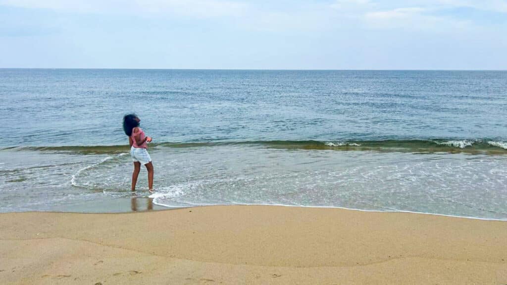 The author Yvette Griffith's daughter posing on the shoreline of the calm Sandy Hook Beach in New Jersey with a clear blue sky in the background