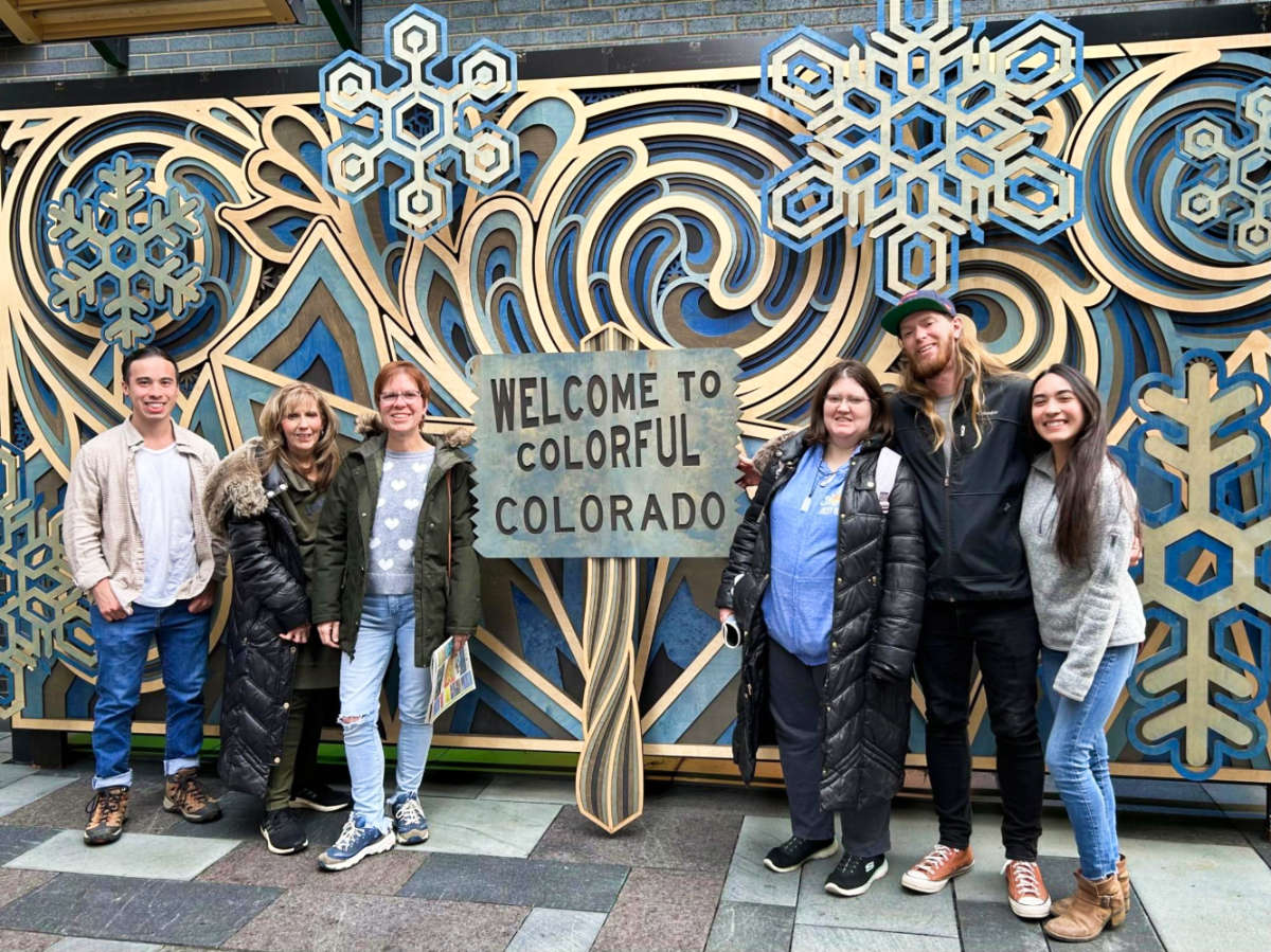 Travel Lemming Editor Abigail Bliss and her family, posing for a photo at the welcome signage in Colorado
