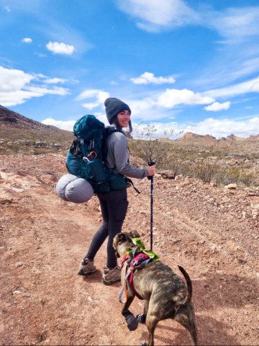 Abigail carrying her Osprey Eja Backpack and accompanied by her dog on the trail