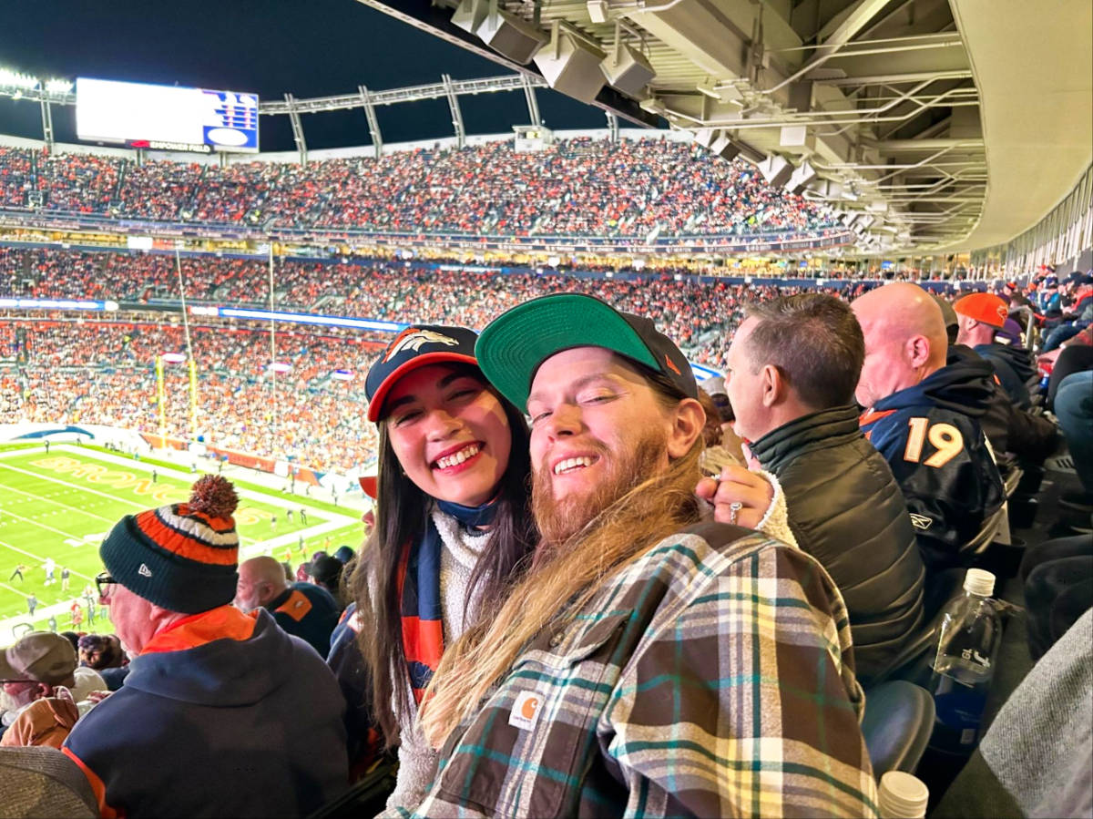 Travel Lemming Editor Abigail Bliss and her husband, smiling for a photo at the Broncos Game