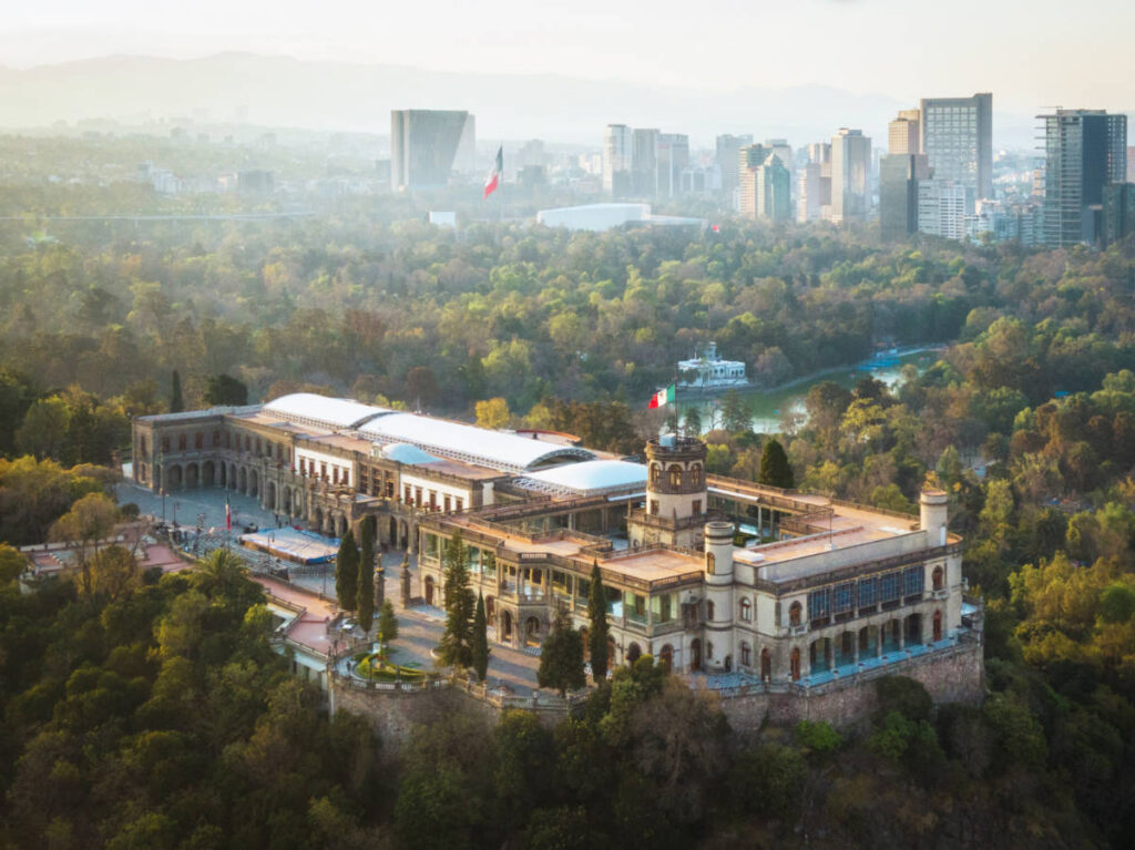 Aerial view of Chapultepec Castle surrounded by greenery with city skyline view in the background