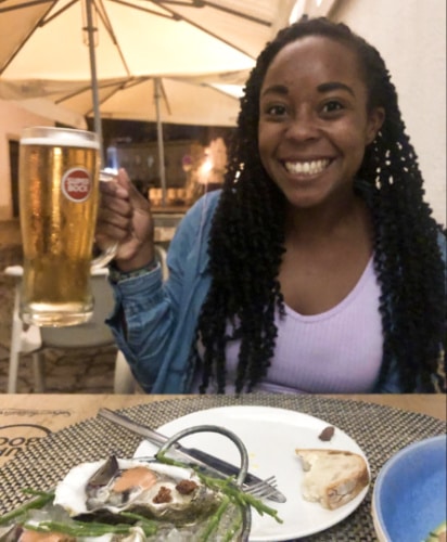 The author Betty Booker smiling brightly while holding a big glass of beer and some seafood dishes on the table at Ai Mãe