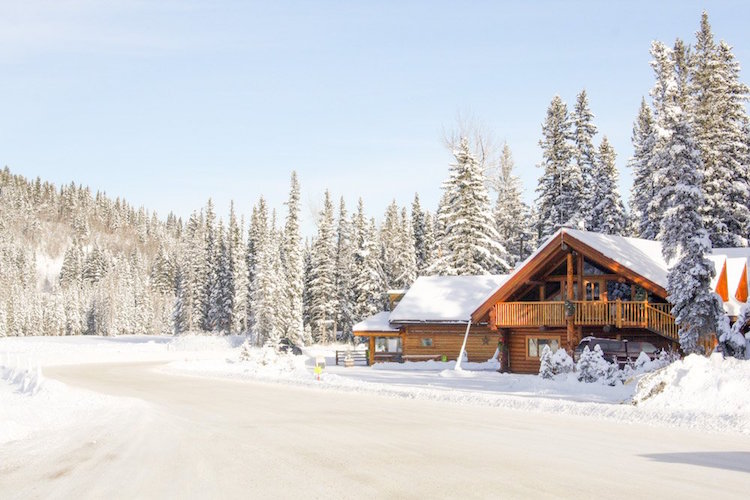 A wooden chalet stands among snowy trees and a road near Cochrane, Alberta Canada
