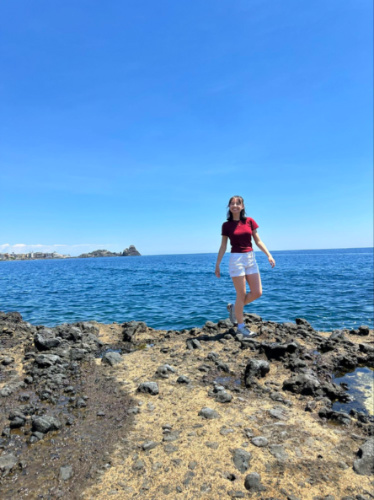 Author Lea Rose walking along the volcanic rock in Aci Castello