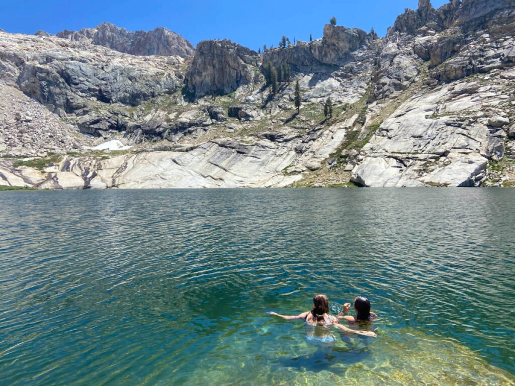 Two people swimming in an alpine lake in the high Sierra Nevada mountains