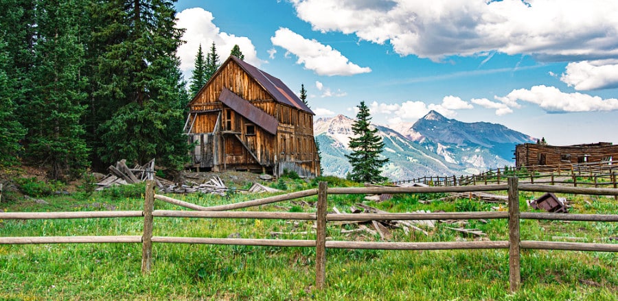 Abandoned wooden buildings surrounded by pine trees with a scenic view at the top of the mountain in Alta, Colorado