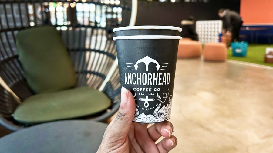 A hand holding a paper cup of Anchorhead Coffee Co in a comfortable lounge