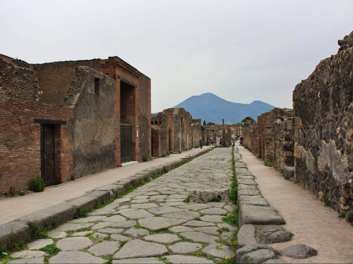 View of the ancient cobblestone streets of Pompeii with the iconic silhouette of Mount Vesuvius