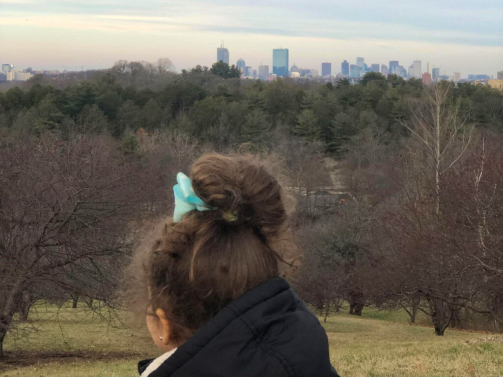 Author Claudicet Pena's daughter gazes at Boston skyline from the Arnold Arboretum of Harvard University