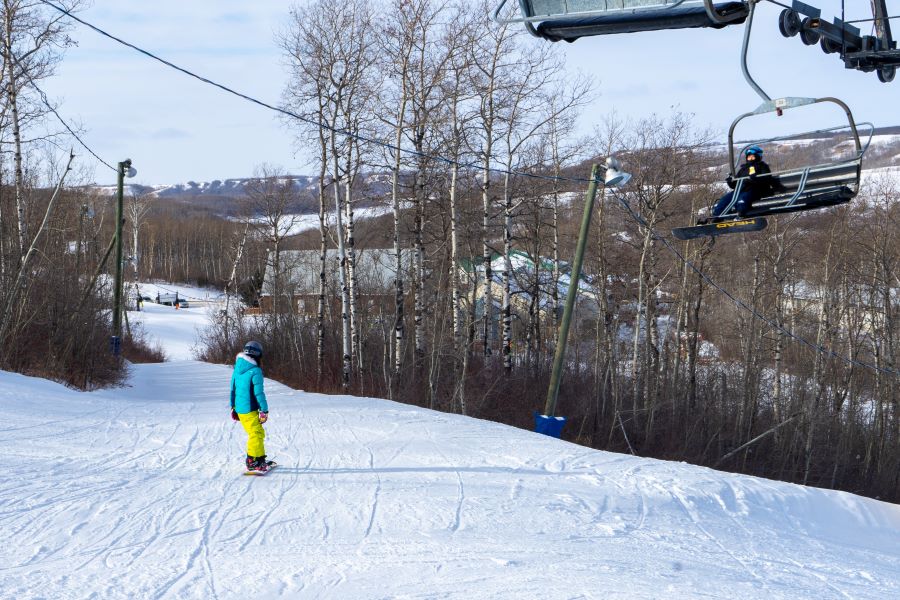 A snowboarder glides as a chairlift goes by in Asessippi Ski Resort