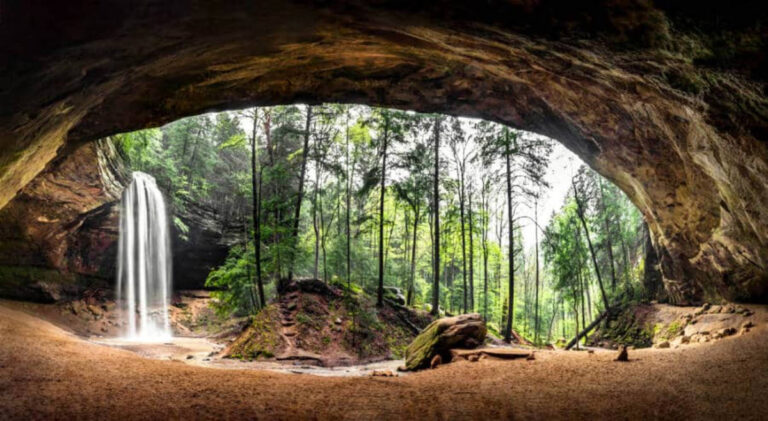 An enormous sandstone recess cave with a waterfall at the entrance
