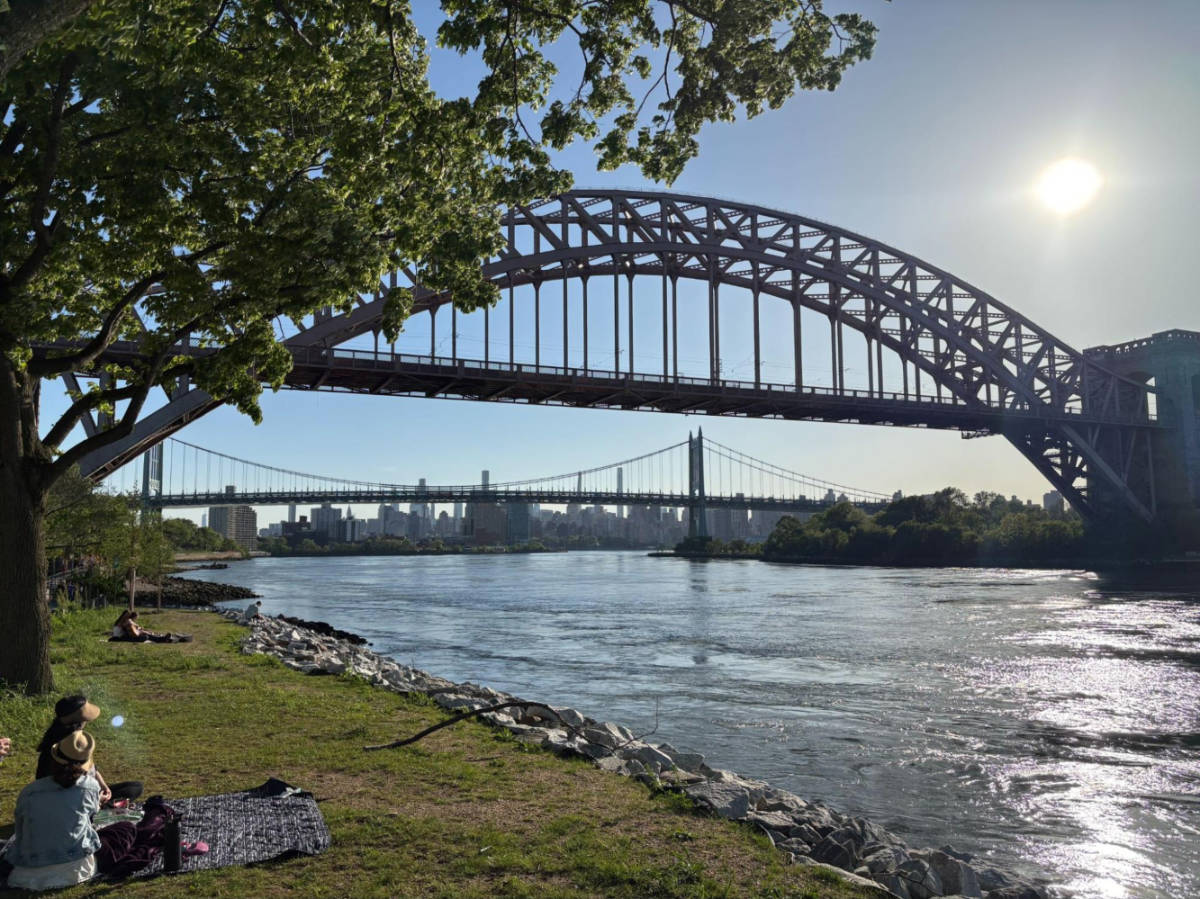 People enjoying the summer day in Astoria Park with the Hell Gate Bridge view from afar