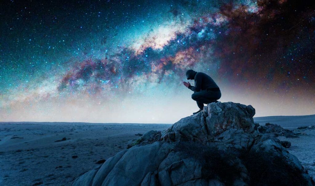 View of a man sitting in Atacama Desert with the Milky Way on his background