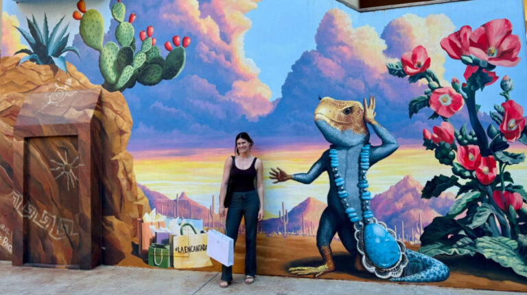Author Betty standing at the mural depicting a whimsical lizard at La Encantada