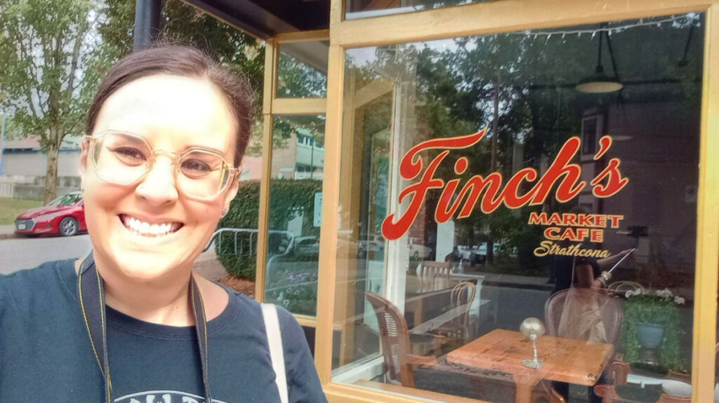 Author Catherine smiling brightly outside Finch’s Market Cafe