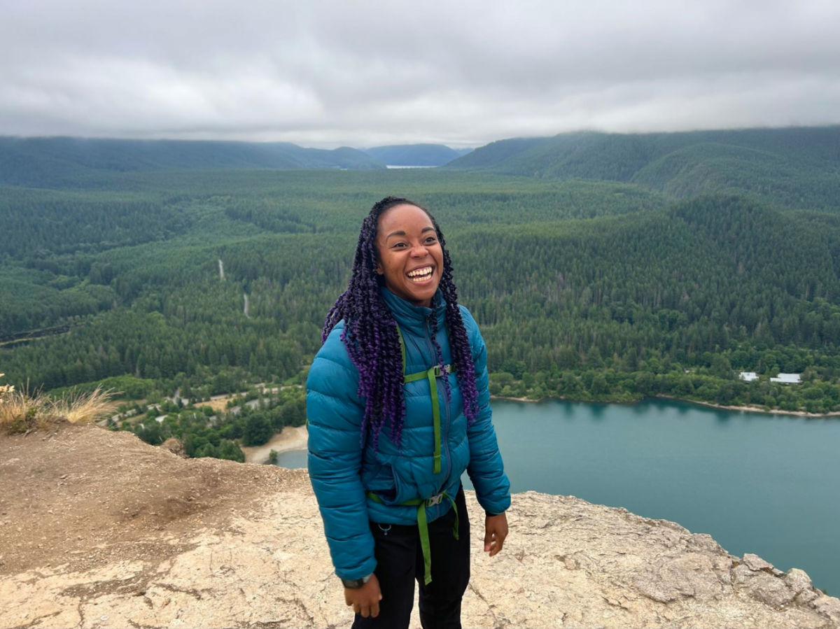 Author Chelsea smiling brightly at Rattlesnake Ledge on a cloudy day