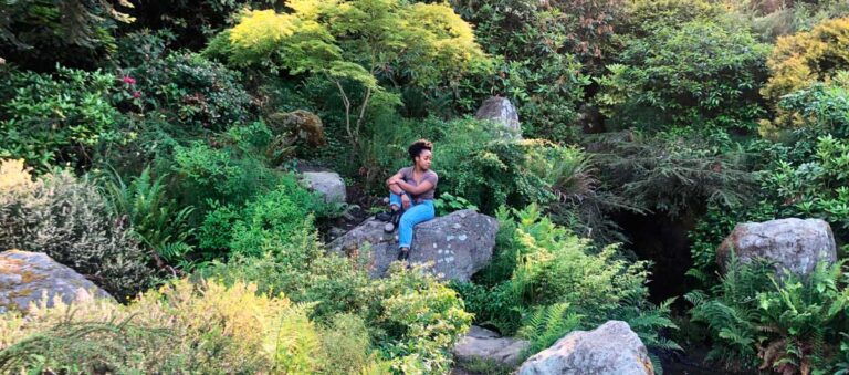 The author Chelsea sitting in a rock surrounded by lush greeneries in Kubota Garden