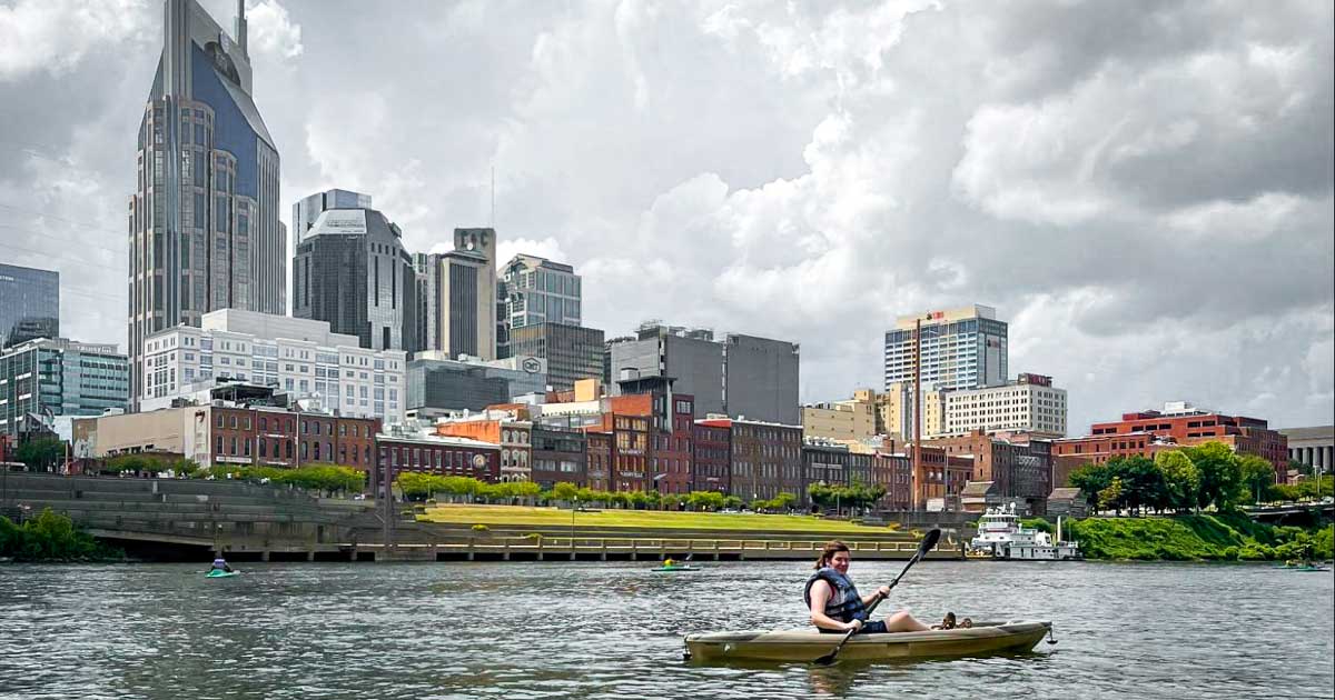 The author kayaking at a river in Nashville with the buildings on her background