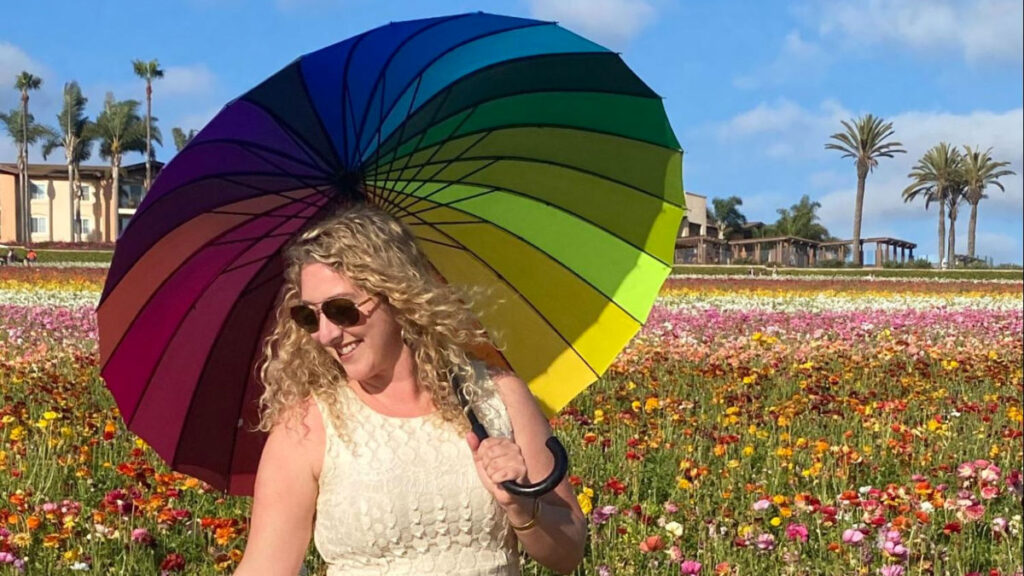 Author Jess holding a rainbow umbrella at the Carlsbad Flower Fields