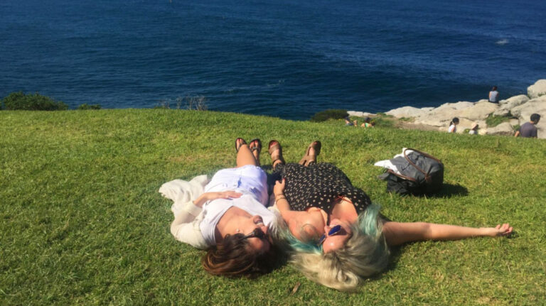 Author Jess and her friend relaxing on the grass by the beach