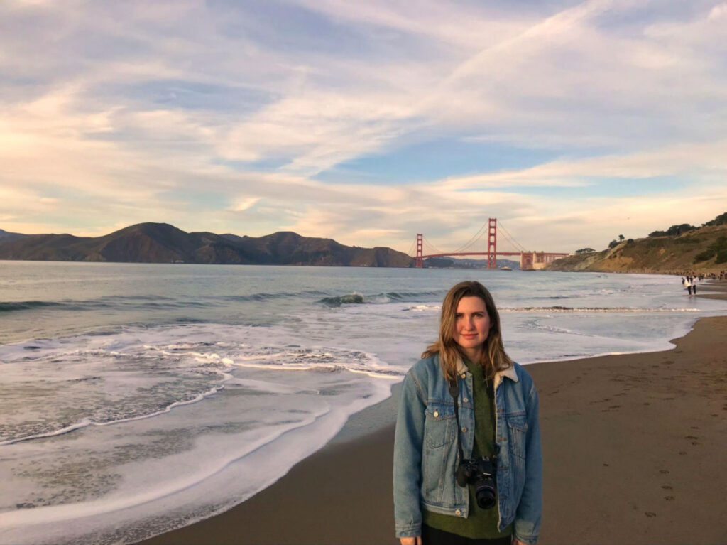 Author Laura standing at San Francisco’s Baker Beach with the Golden Gate Bridge in the background