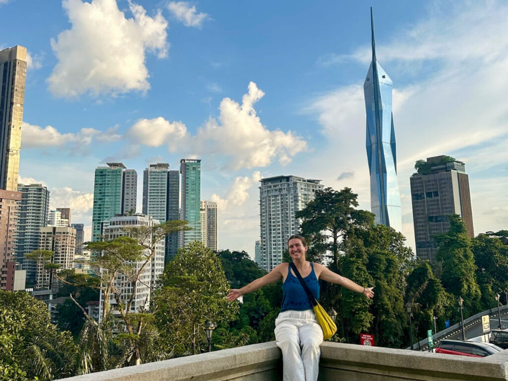 Author Laura sitting in front of the downtown skyline with Merdeka 118 in the background