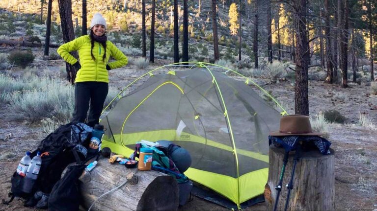 Author McKenna wearing a yellow jacket stands beside a tent