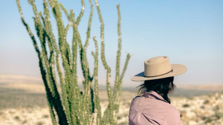 Author McKenna wearing a hat stands beside a cactus while looking at the view