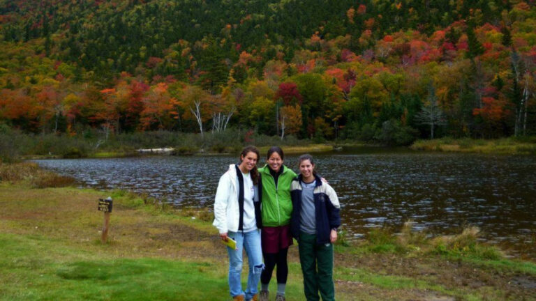 Author Meg and her friends stand by a serene lake surrounded by vibrant fall foliage in the Berkshires