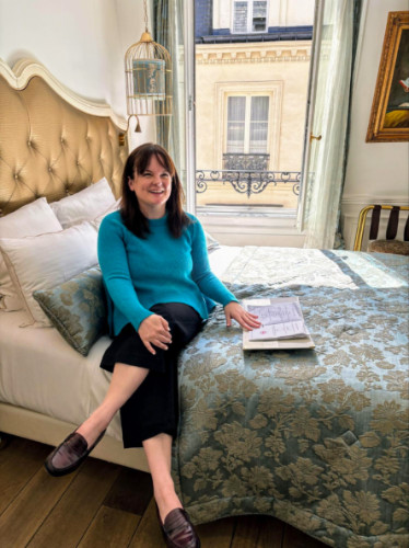 Author Rachel perusing the welcome book on the cozy bed of Hôtel Académie Saint-Germain