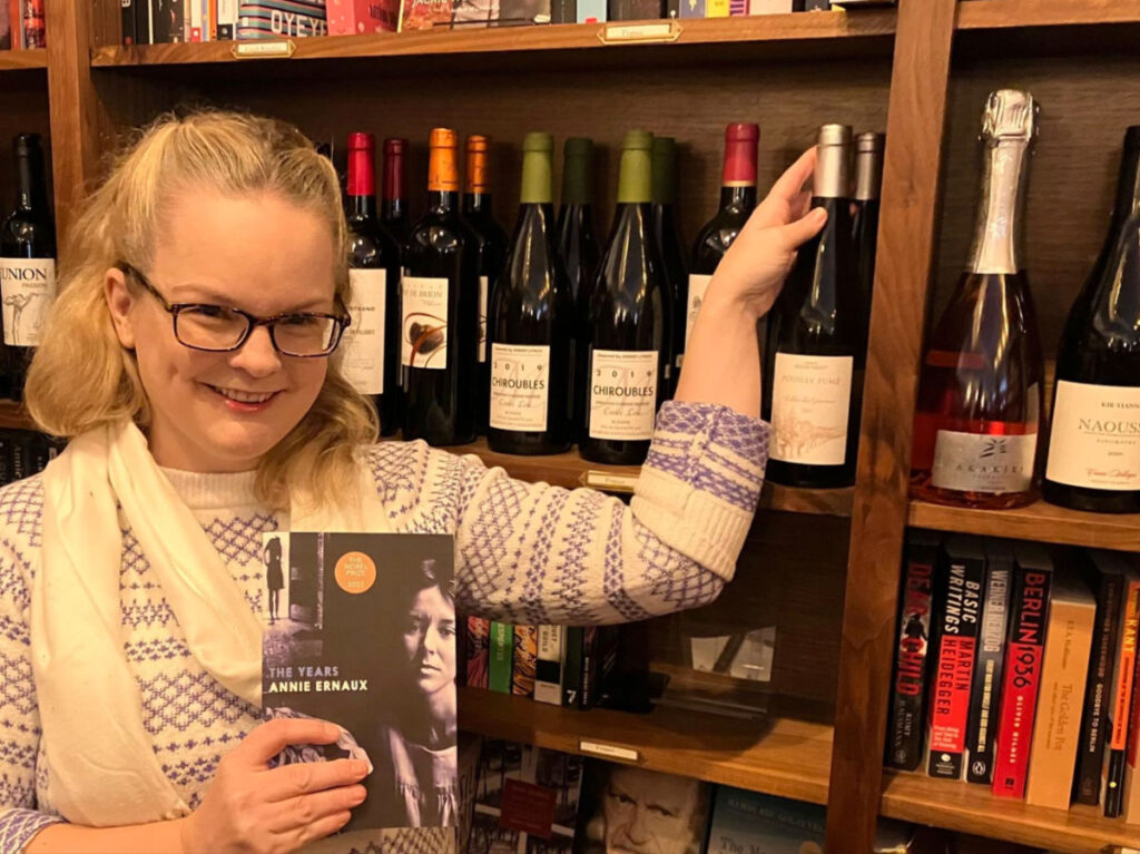 Author Rachel holding a book and bottle of wine at the France shelf of Leopold's