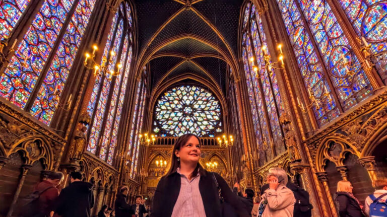 Author Rachel at the upper chapel of Sainte-Chapelle in Paris, surrounded by towering stained glass windows and Gothic arches