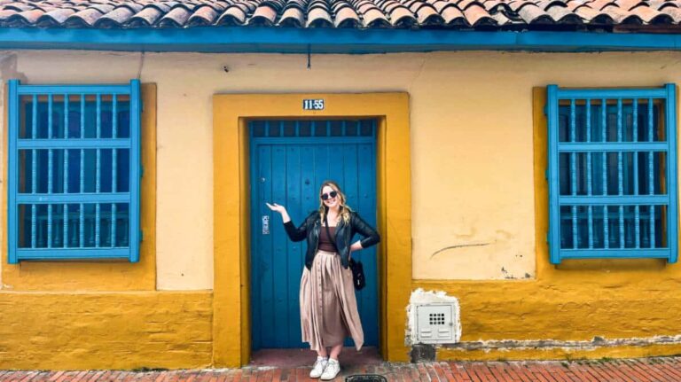 The author Taylor Herperger, posing in front of a blue door on a yellow house in Bogota