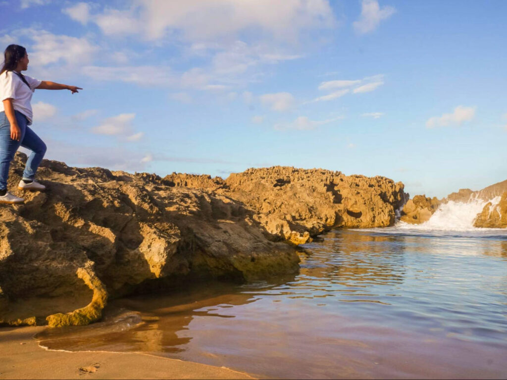 Author Vanessa pointing at the sea while standing on a rock at the beach in April