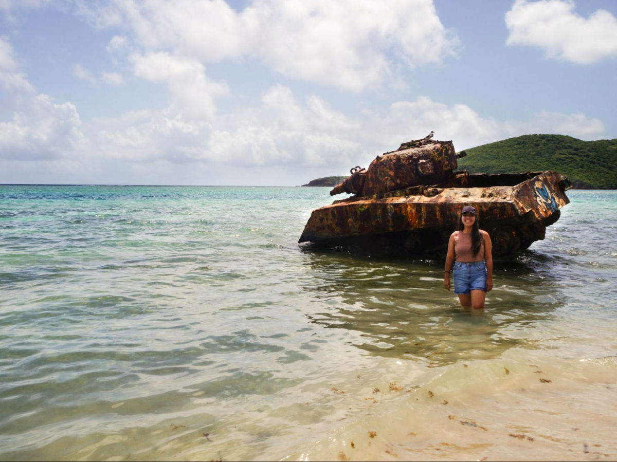 Author Vanessa standing next to an old and rusty tank at Flamenco Beach