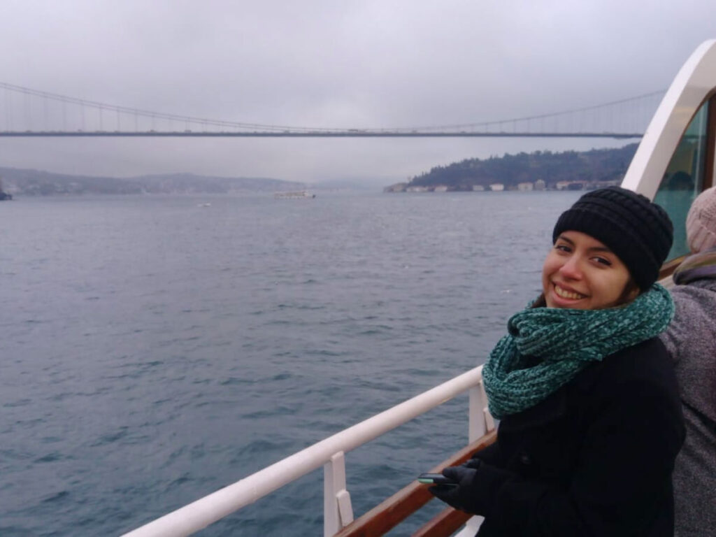 Author Vanessa in a black coat, green scarf, and knit hat stands on the deck of a ferry