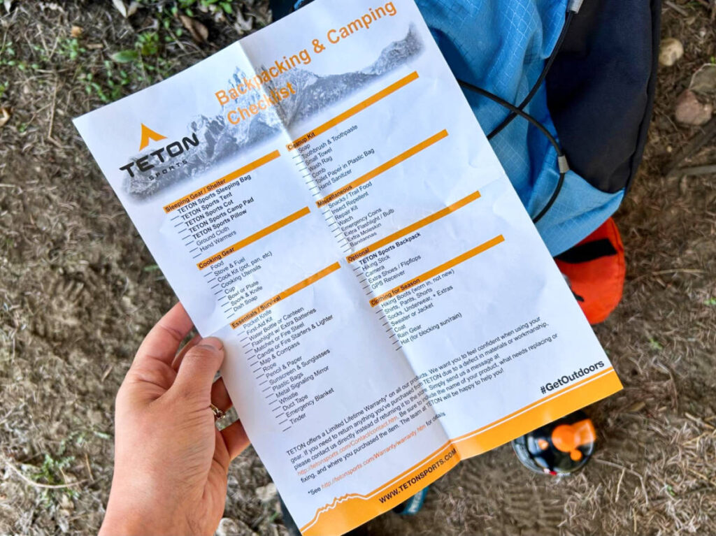 A hand holding a paper with a backpacking and camping checklist