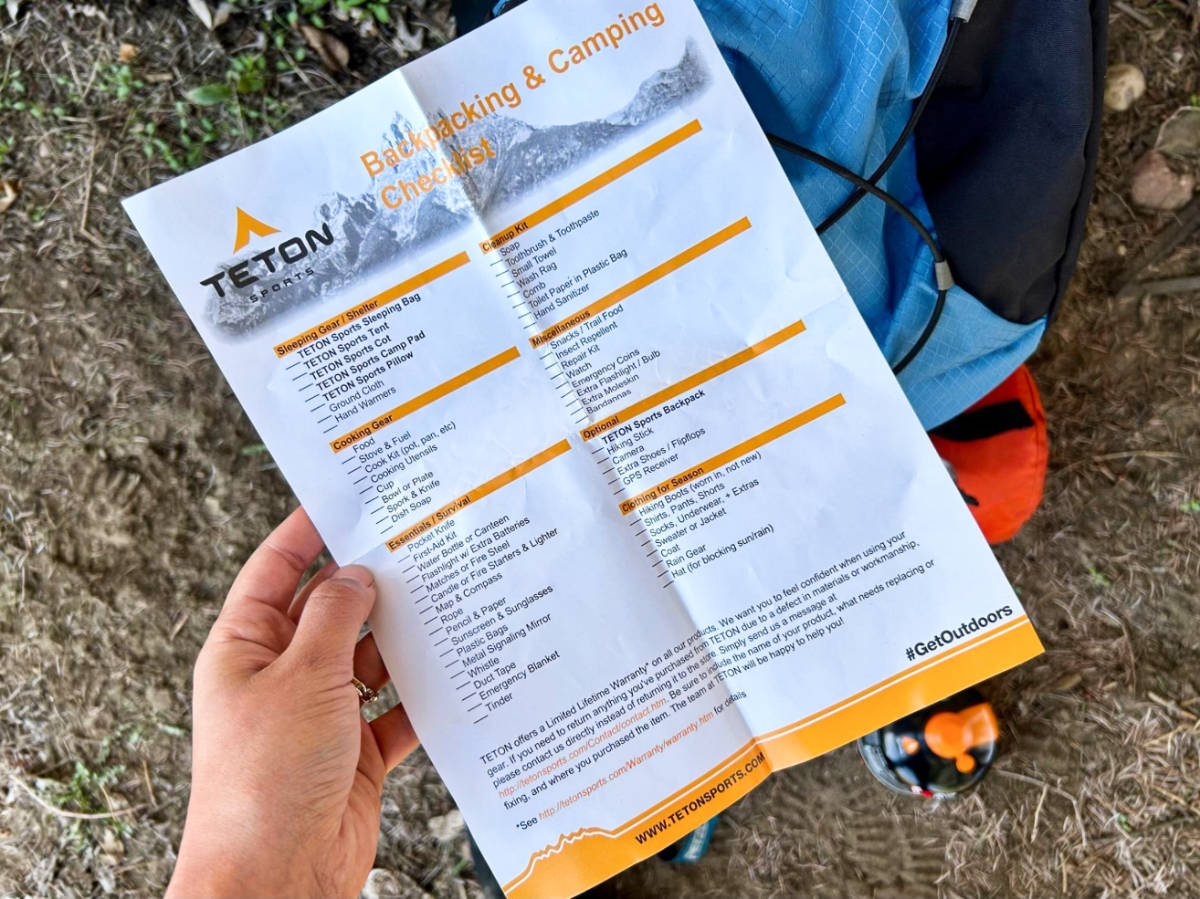 A hand holding a paper with a backpacking and camping checklist