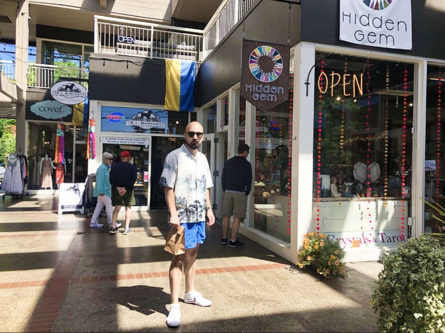 A man posing outside the shops in Bainbridge Island with people wandering around in the background