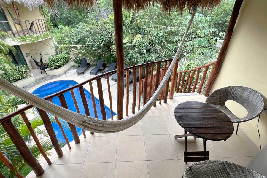 Table, chair, and a hammock with a pool view at the balcony of a room in Hotel Villas Akalan