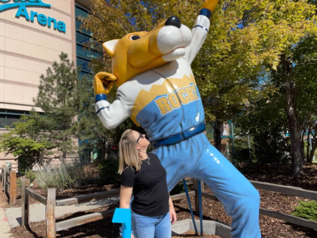 The author, Laura Falin with the statue of Rocky the Mountain Lion outside Ball Arena