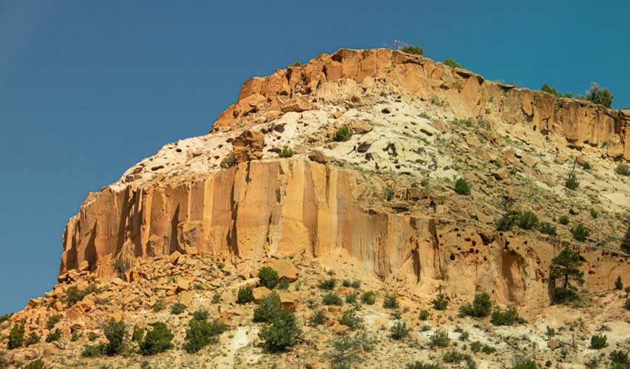 Scenic view of a large rock formation with bushes at Bandolier National Monument