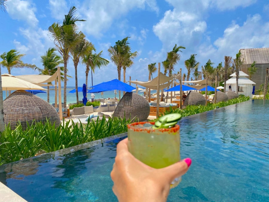 A hand holding a glass of alcoholic drink by the pool