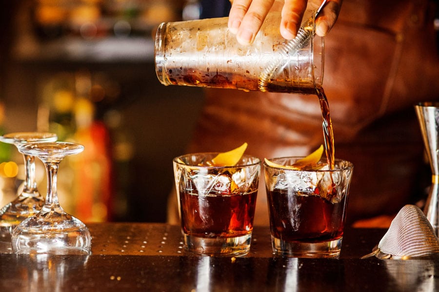 View of a bartender pouring an alcoholic drink on a glass with ice cubes