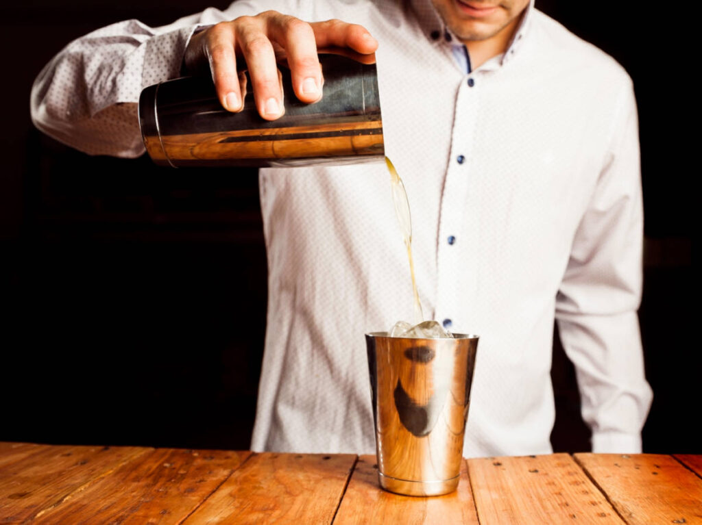 A bartender pouring alcohol into a glass shaker