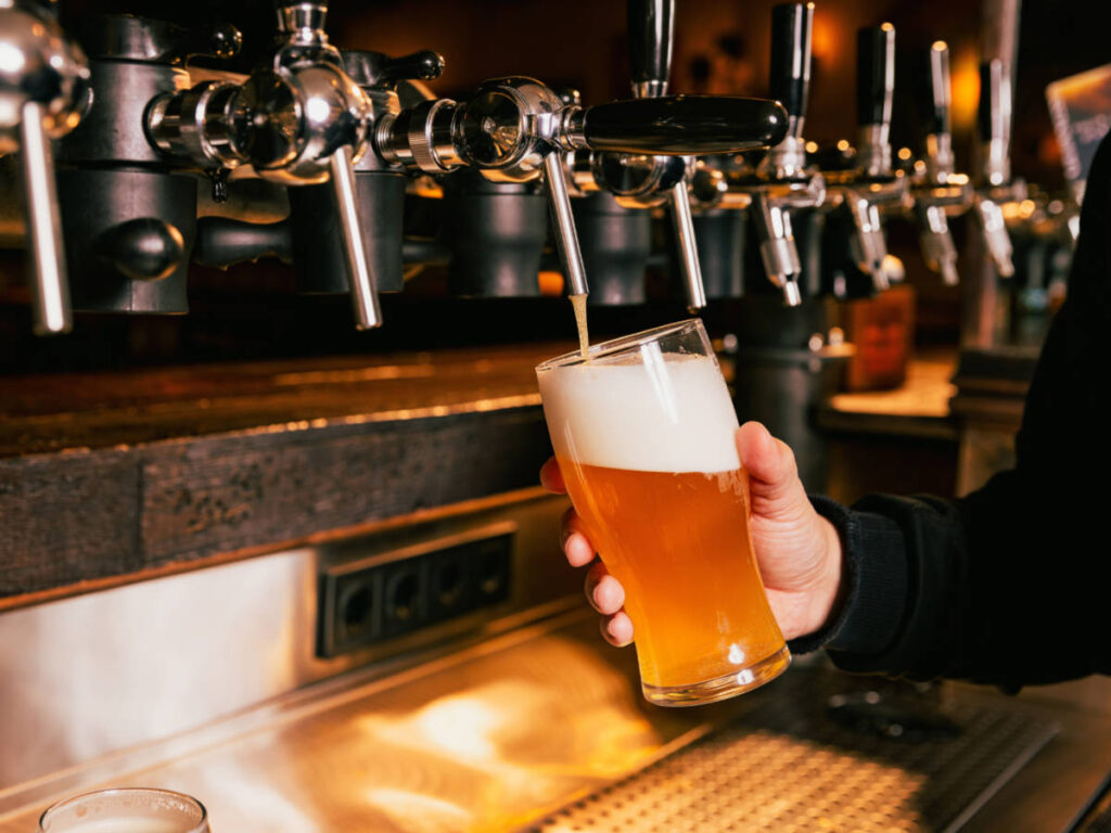 A hand pouring cold foamy beer from tap into glass
