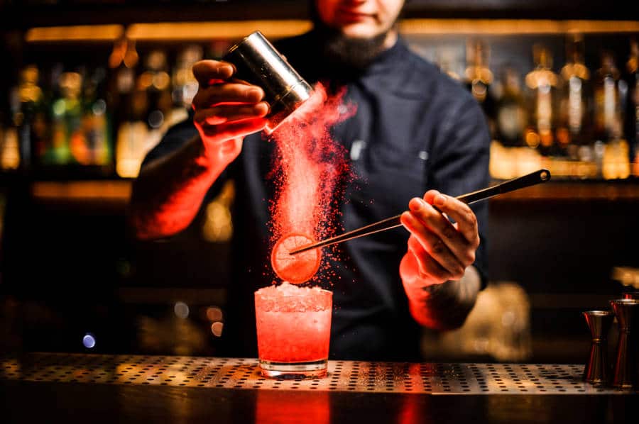 A bartender adding powdered spice into a sliced lemon and cocktail drink