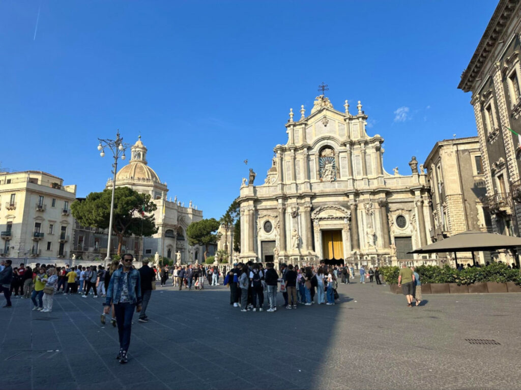 A group of people strolling in a square with Basilica Cattedrale di Sant'Agata visible