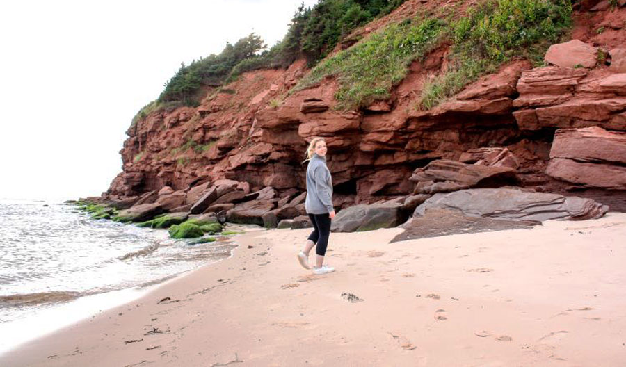 The author stands on the beach in front of a red cliff in Basin Head Beach, PEI